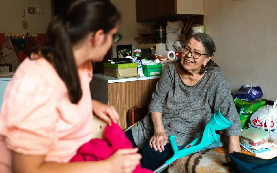 Caregiver helping an older woman put on a pink sweater at home