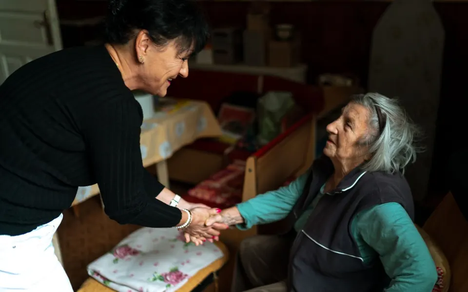 Caregiver shaking hands with an older woman in a living room