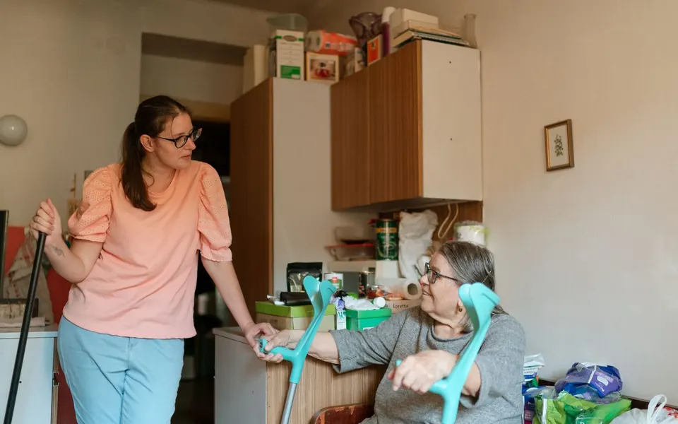 Caregiver walking beside an older woman using crutches at home