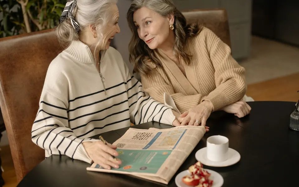 Two women laughing together over a crossword puzzle